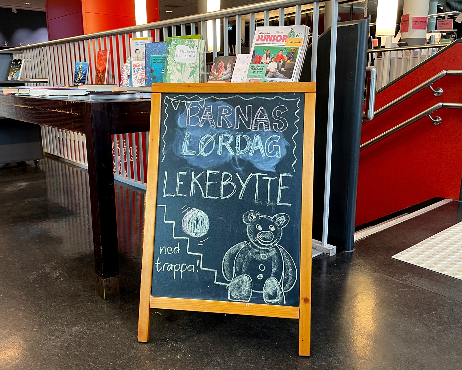 En tavle hvor det er tegnet "Barnas lekebyttedag" inne i biblioteket