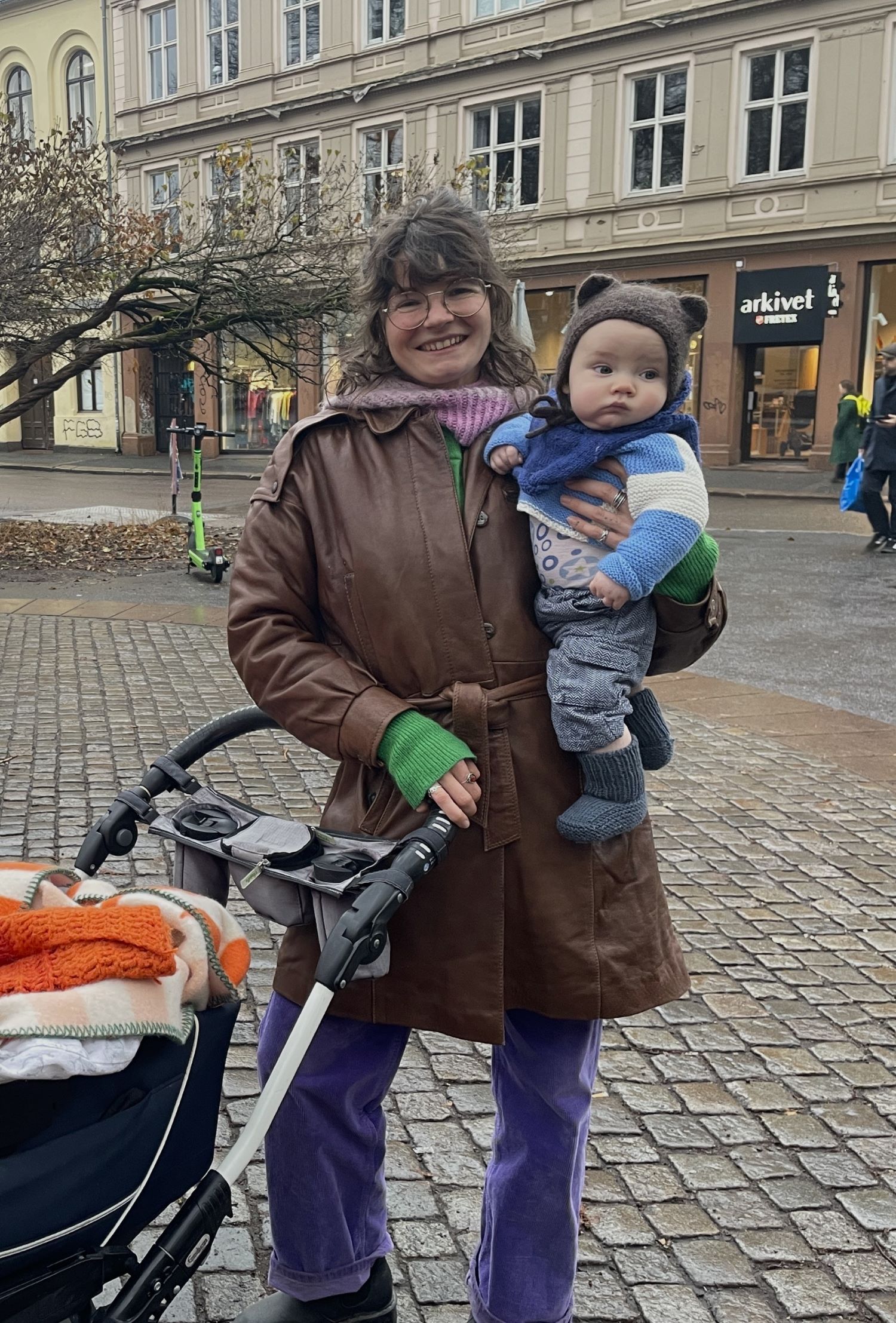 Matja Kostveit står på Olaf Ryes Plass foran barnevognen sin. Hun holder sønnen Reodor i armene.