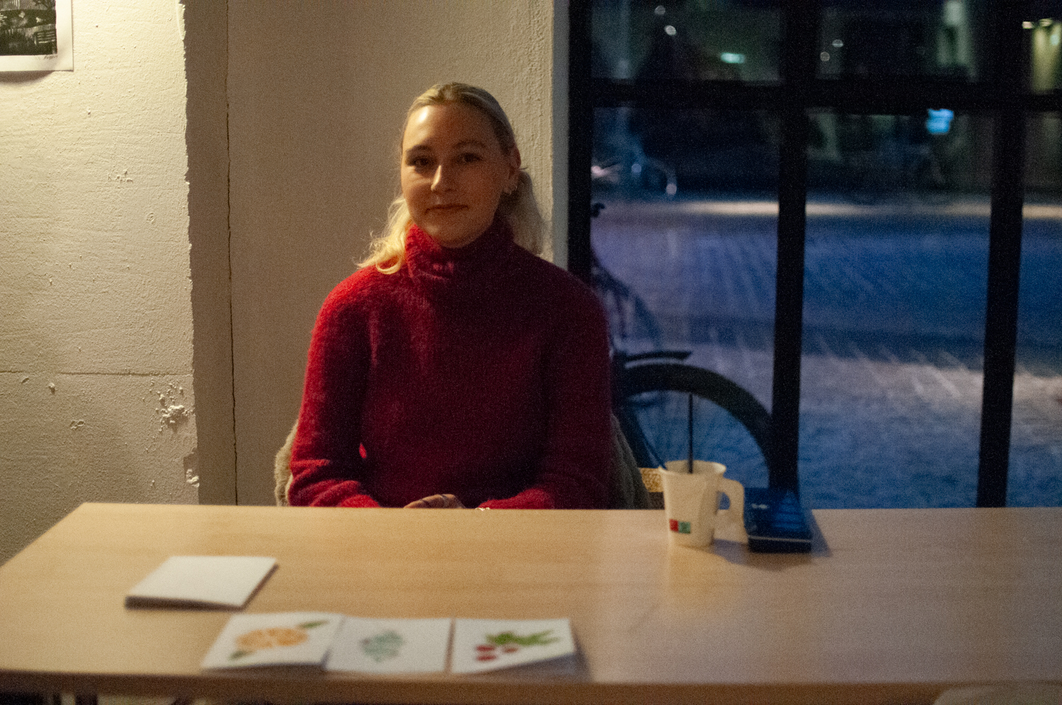 En kvinne med rød genser sitter bak et bord. På bordet ligger tre julekort. 