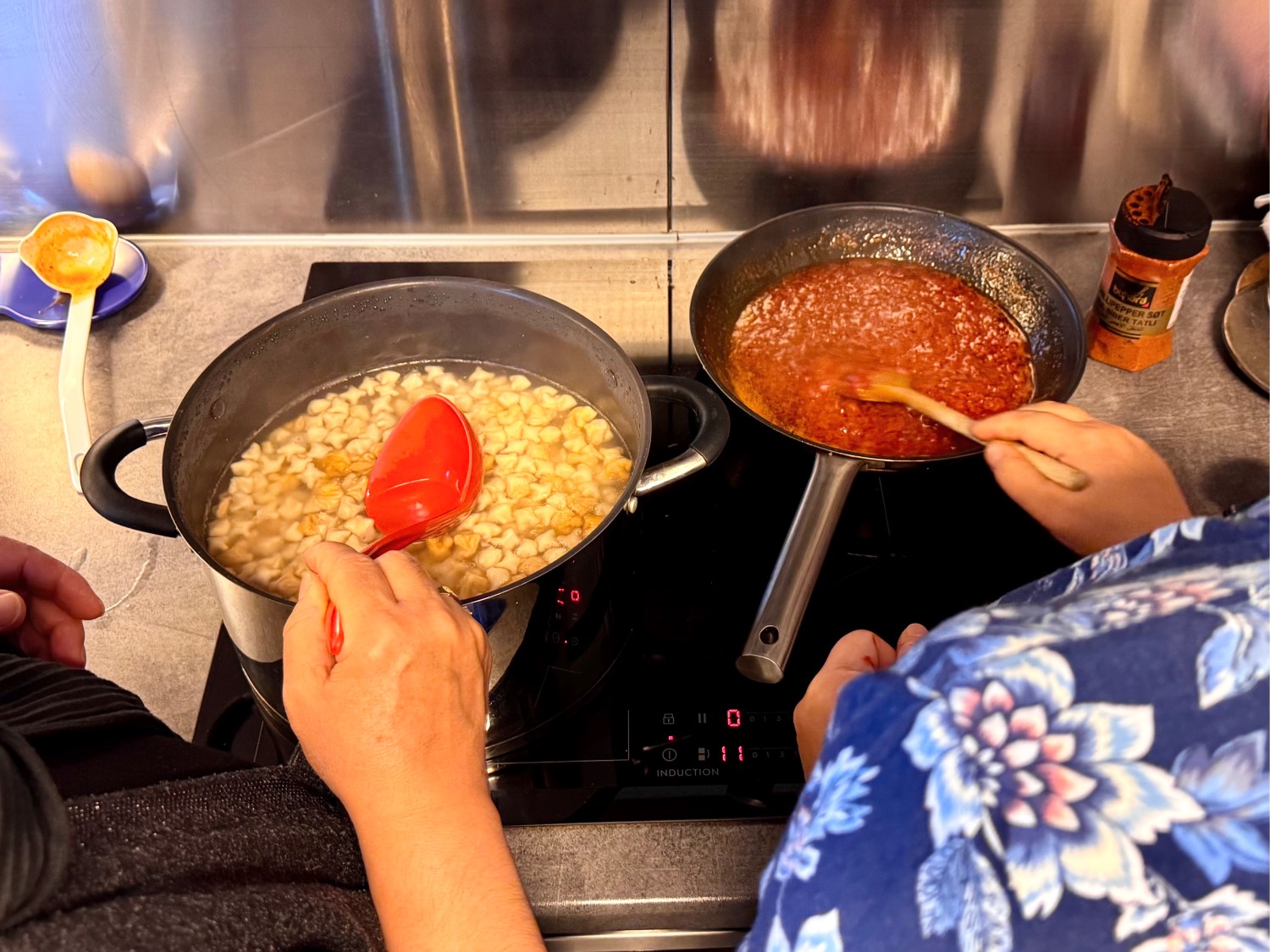 Tyrkisk tortellini som lages i to kjeler. Bildet er tatt ovenfra, bak skuldrene til to av damene som står og rører rundt i kjelene på komfyren. 