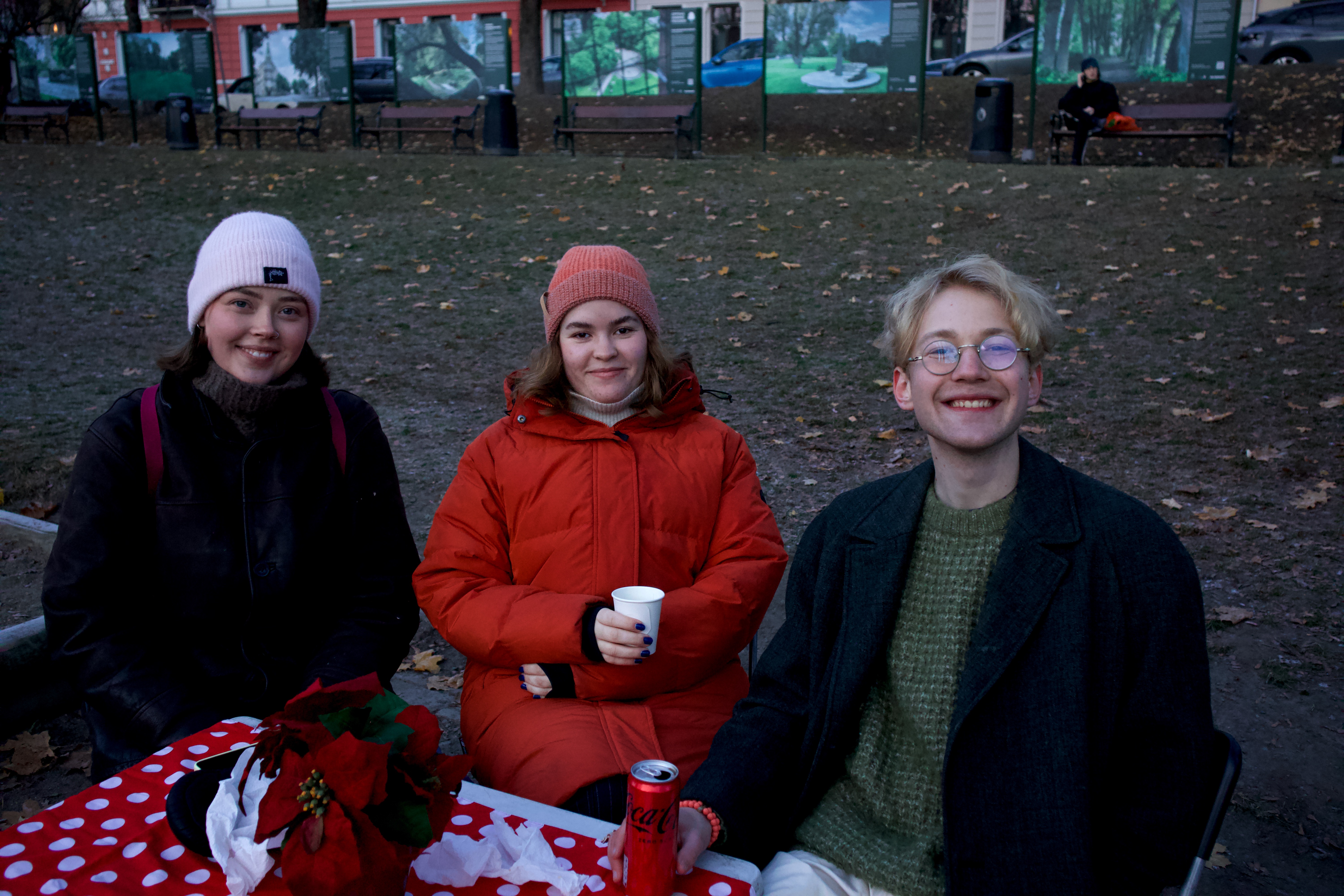 Tre venner sitter rundt et bord og drikker kaffe på markedet. De smiler til kameraet