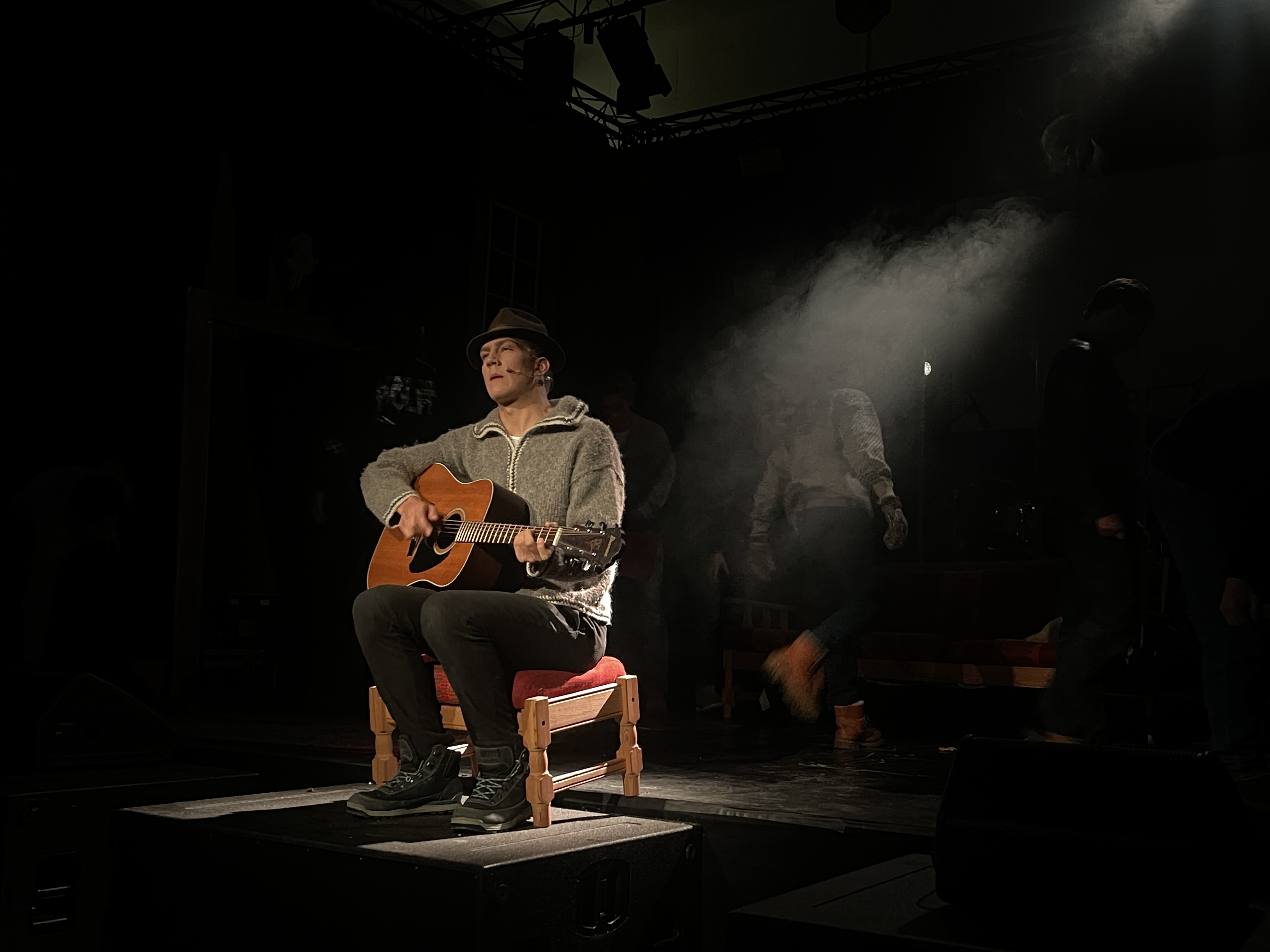 En av skuespillerene sitter alene på scenen med gitar og synger