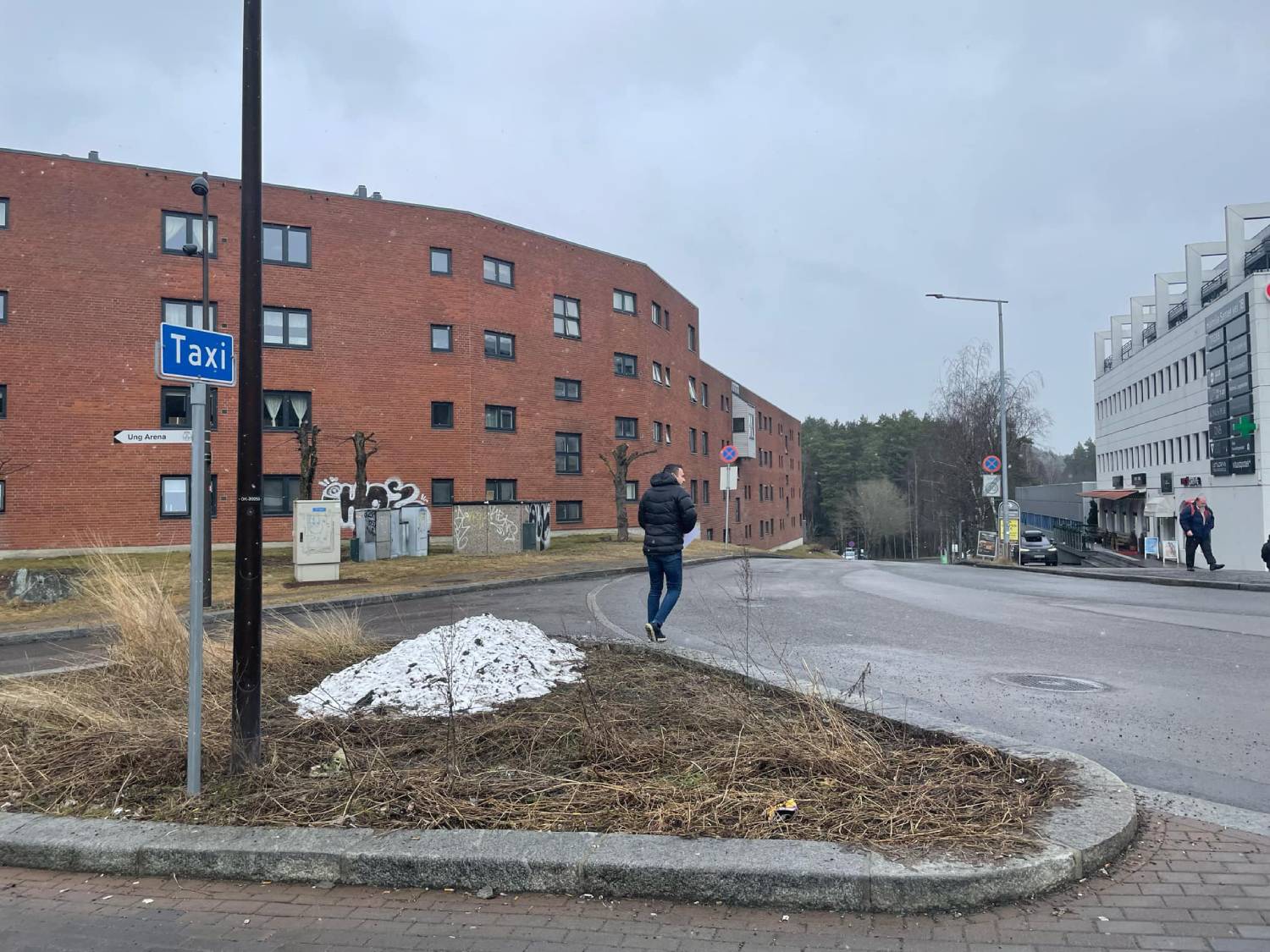 En mann går forbi en liten snøfonn på Holmlia