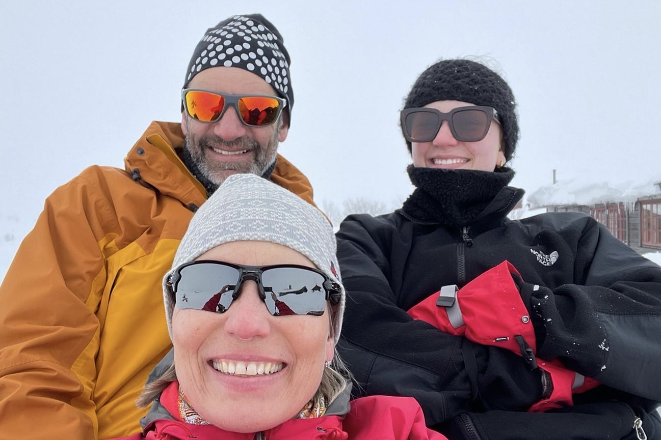 Familie på tre som smiler med solbriller og lue på.