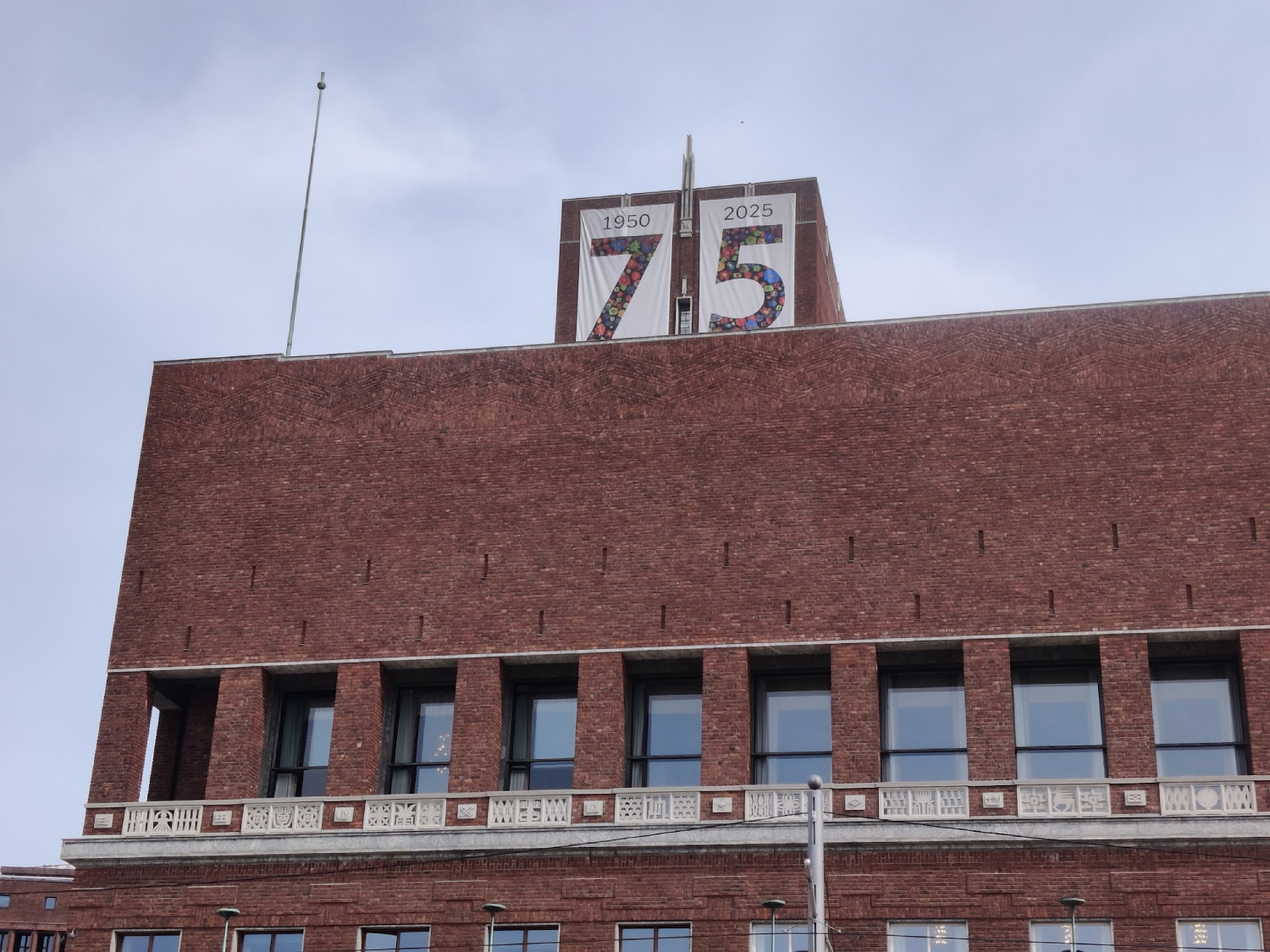 En murbygning i forgrunn med en plakat der det står "75". Blå himmel i bakgrunnen.