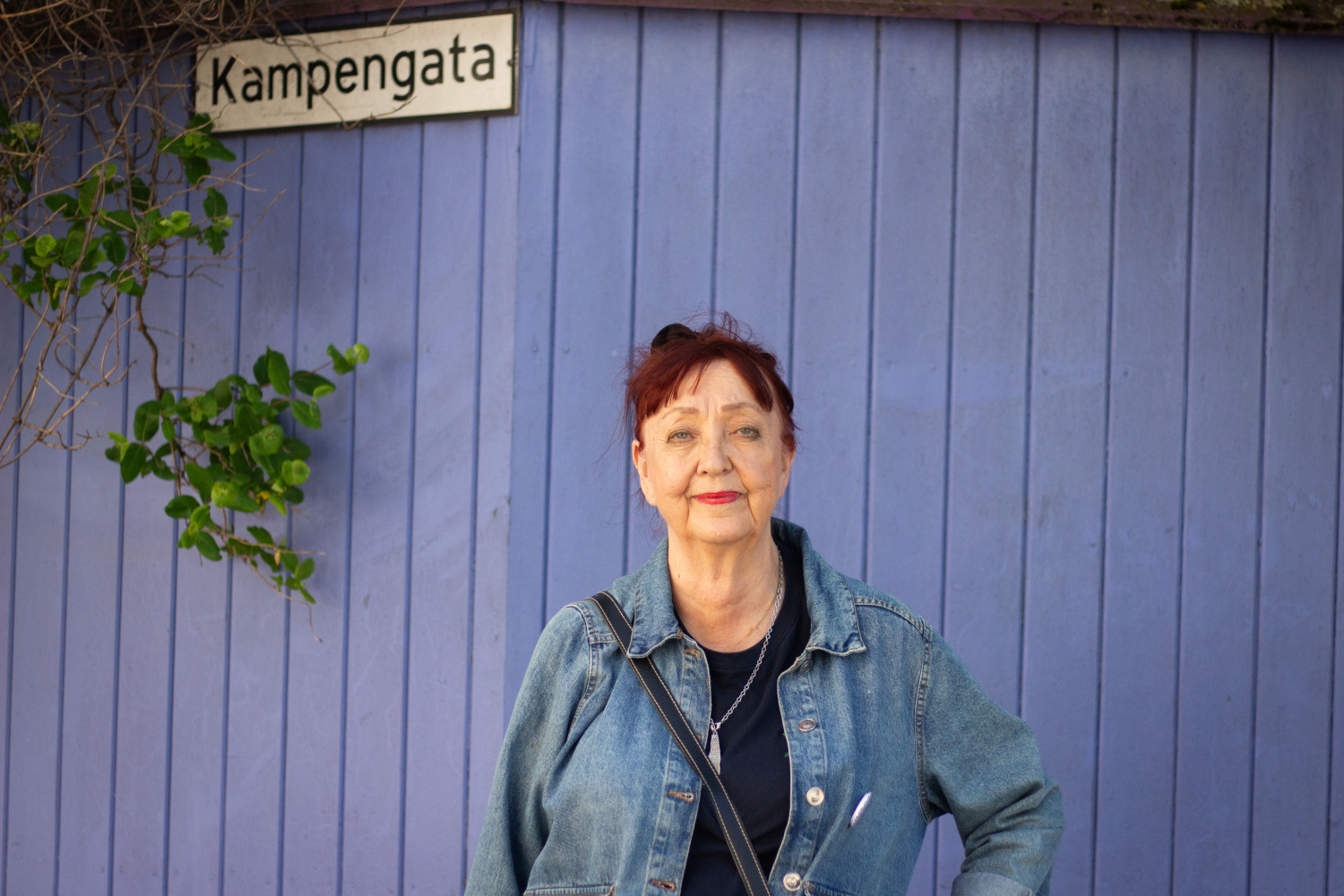 Bilde av en eldre dame foran en lilla vegg. Hun smiler forsiktig.