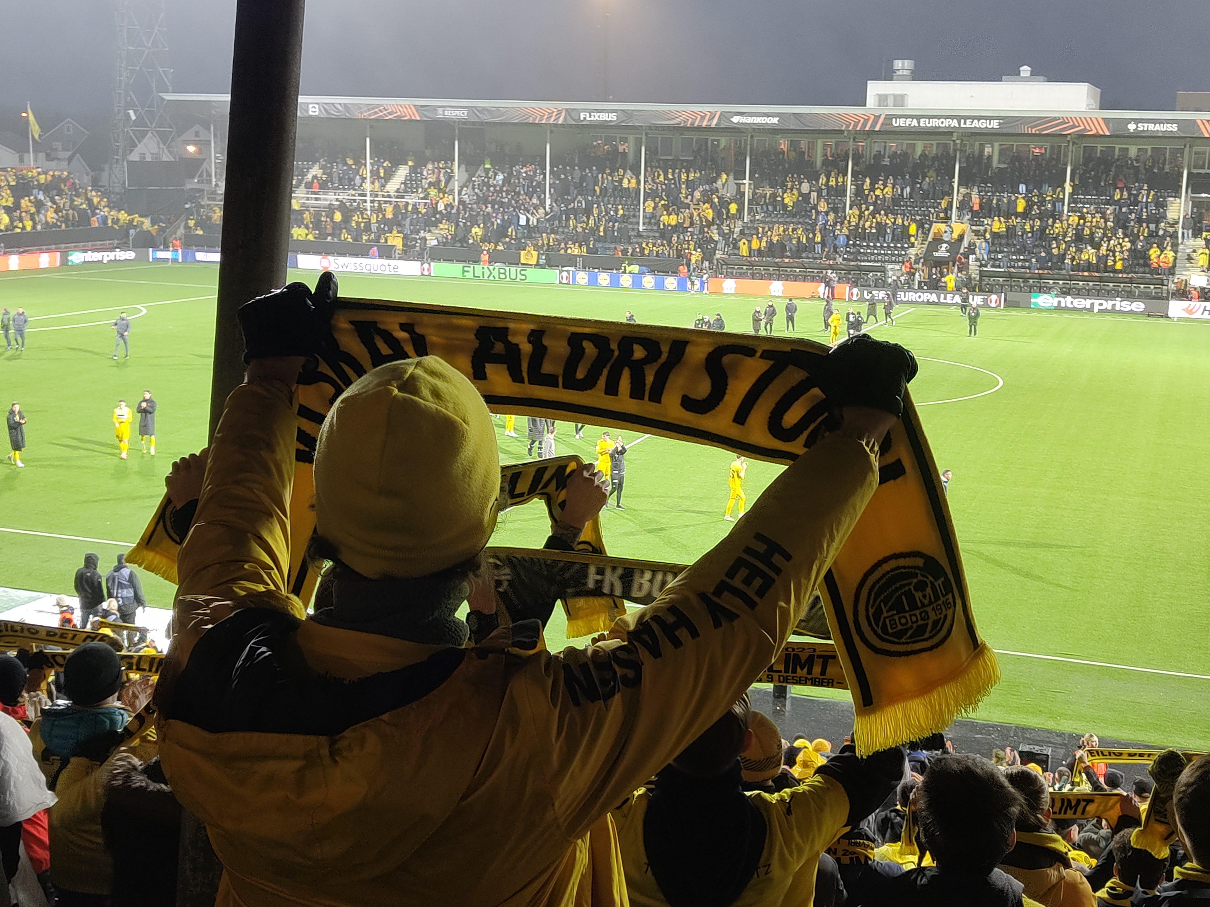 "Vi skal aldri stoppe" står skrevet på flagget som veives høyt av Bodø/Glimt-supporterne