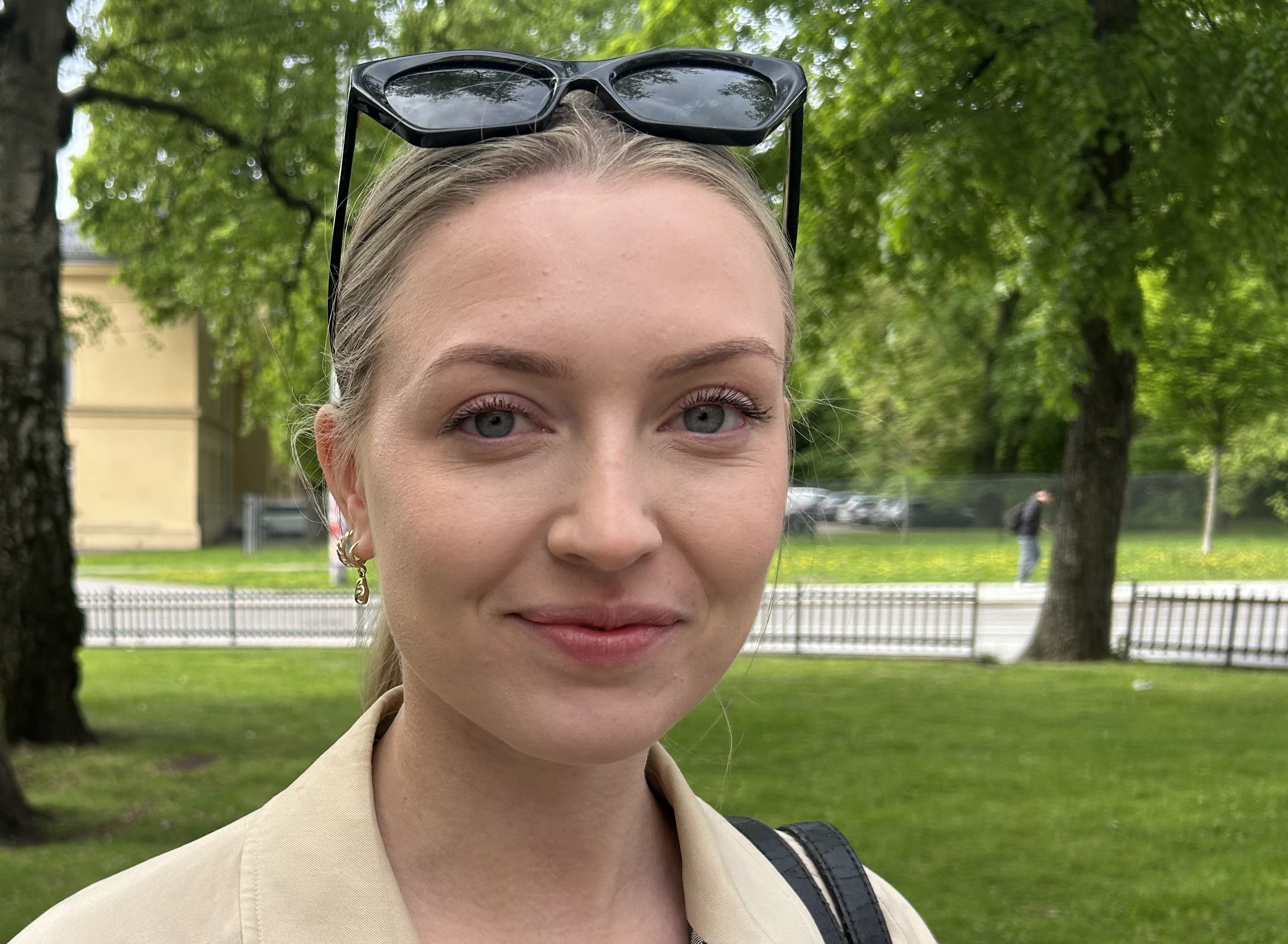 Ung dame som smiler med grønn natur i bakgrunnen imens hun venter på bussen.
