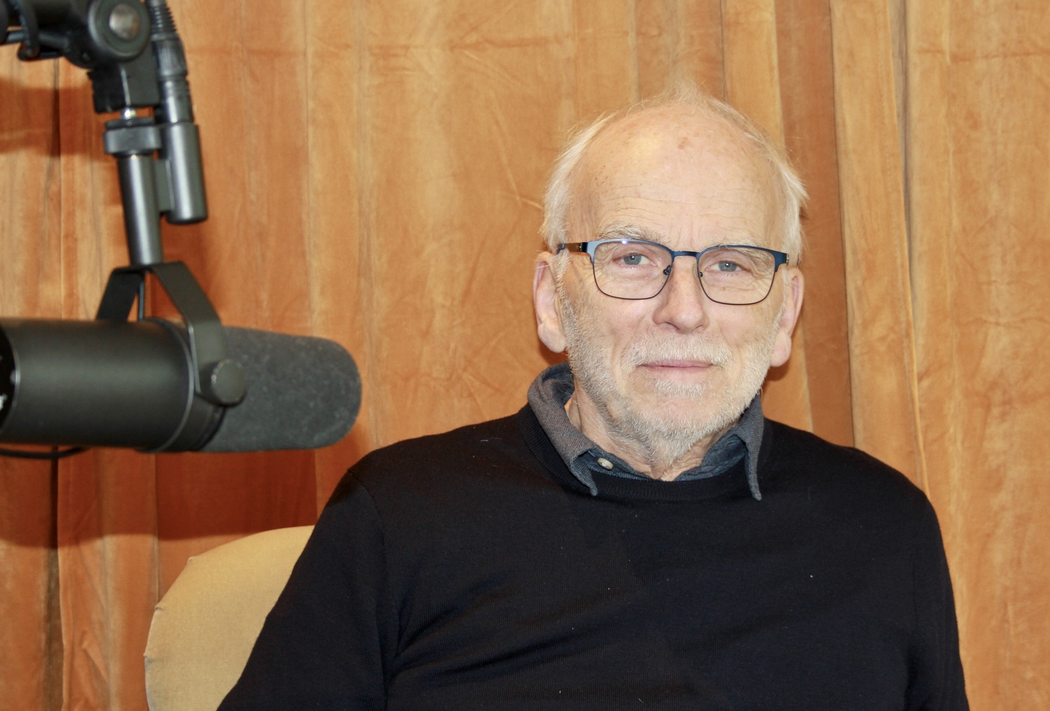 Professor Sverre Varvin sitter i et podkaststudio med en svart mikrofon og eikevegger.