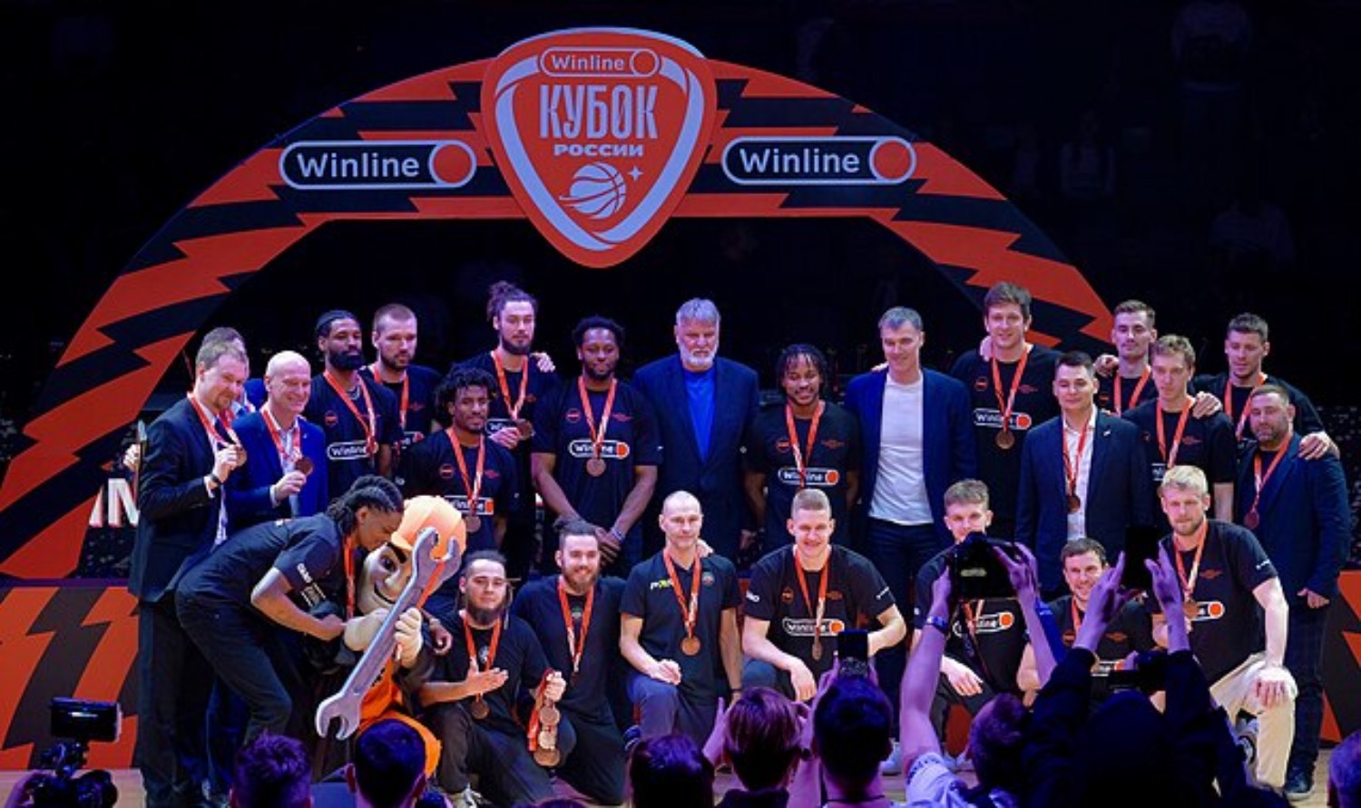 Et basketballag smiler foran en oransje vegg