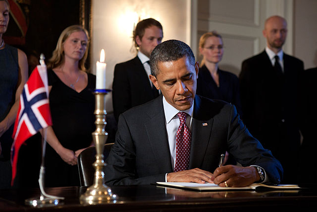 Obama sitter og skriver under en avtale med et norsk flagg i bakgrunnen