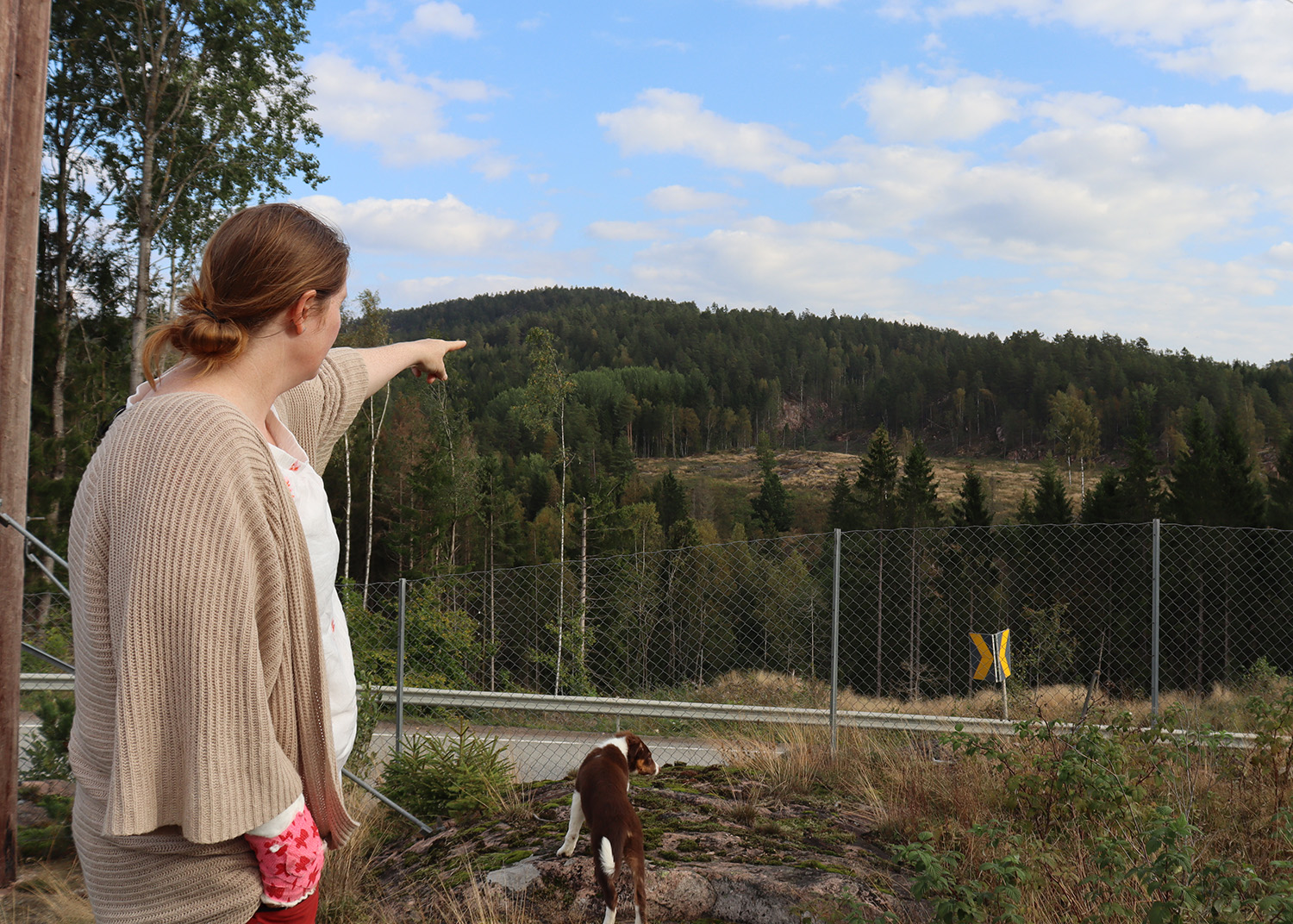 Dame står på en fjellknaus og peker utover landskapet.