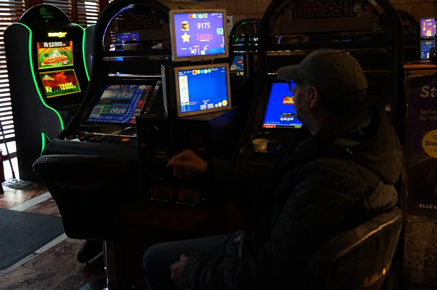 Mann sitter delvis med ryggen til foran en bingoskjerm
