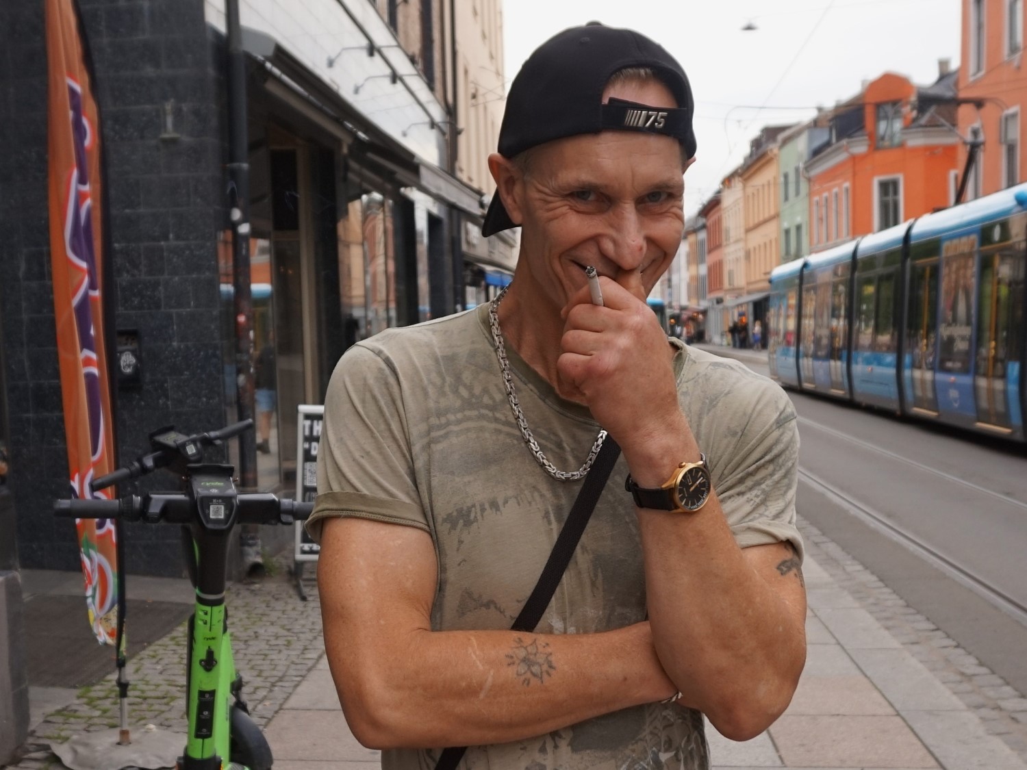 En mann med caps smiler med en sigarett i hånda