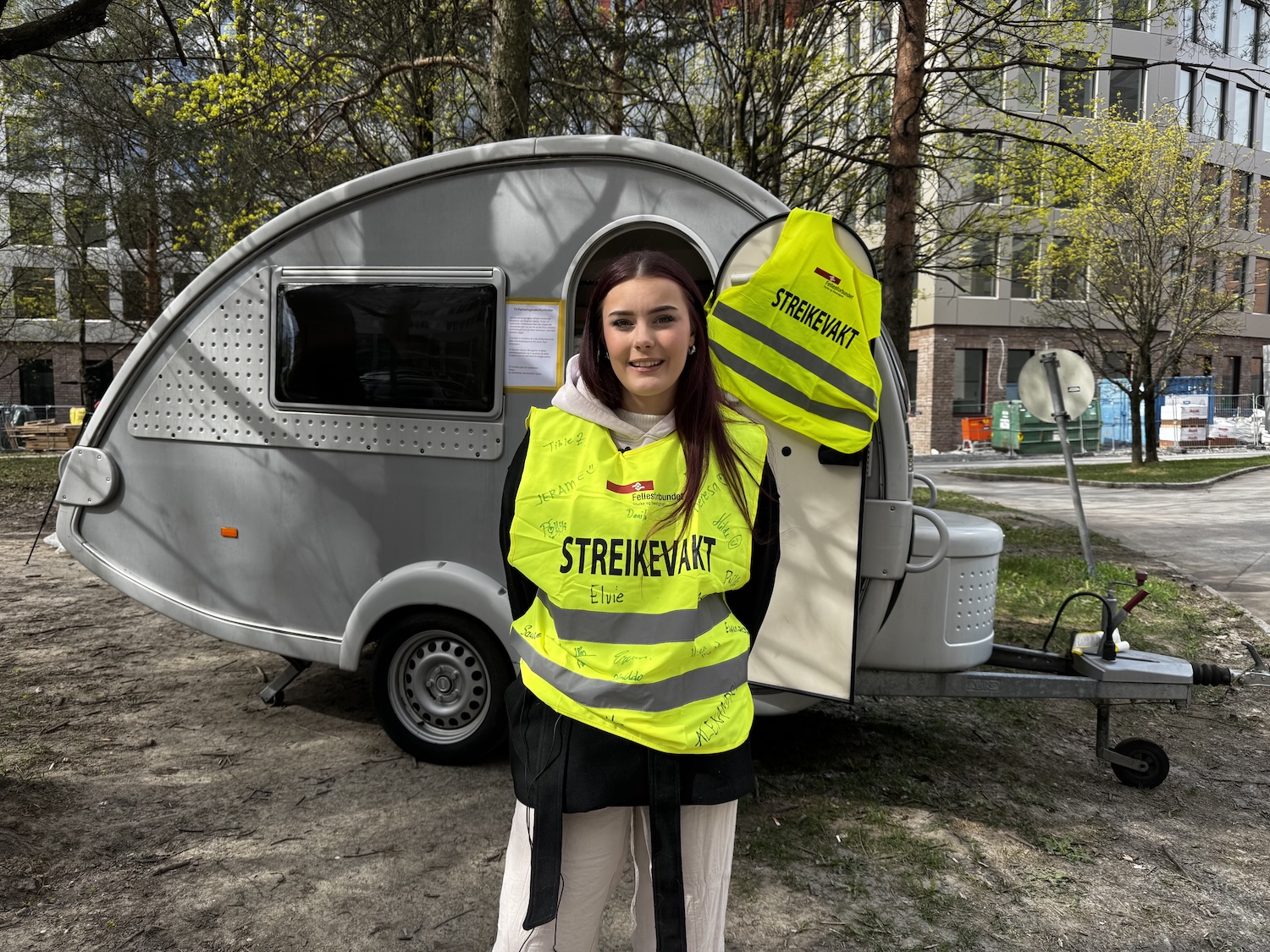 Jente med gul streikevest foran en campingvogn 