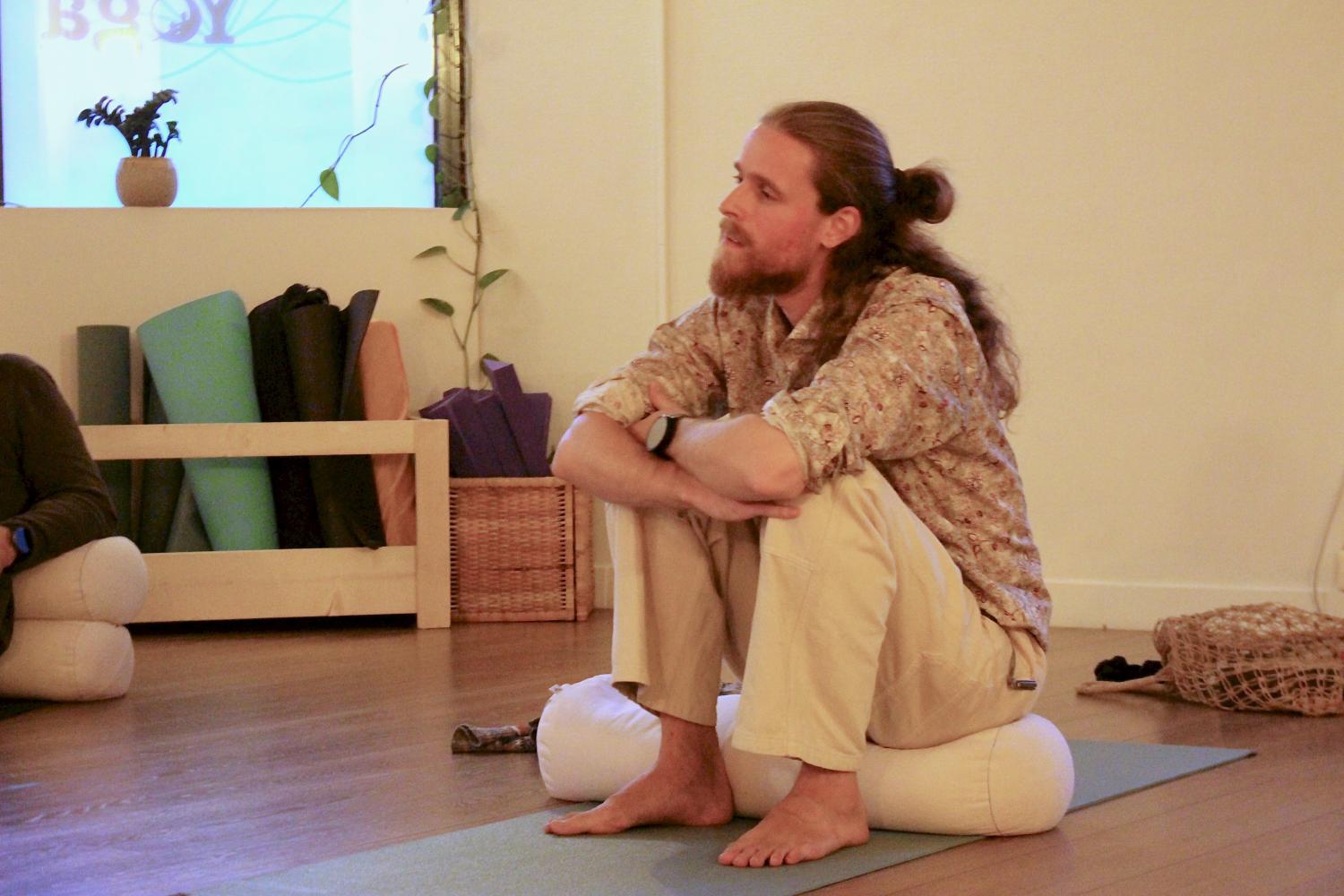 Mann med langt hår og manbun sitter på en yogamatte