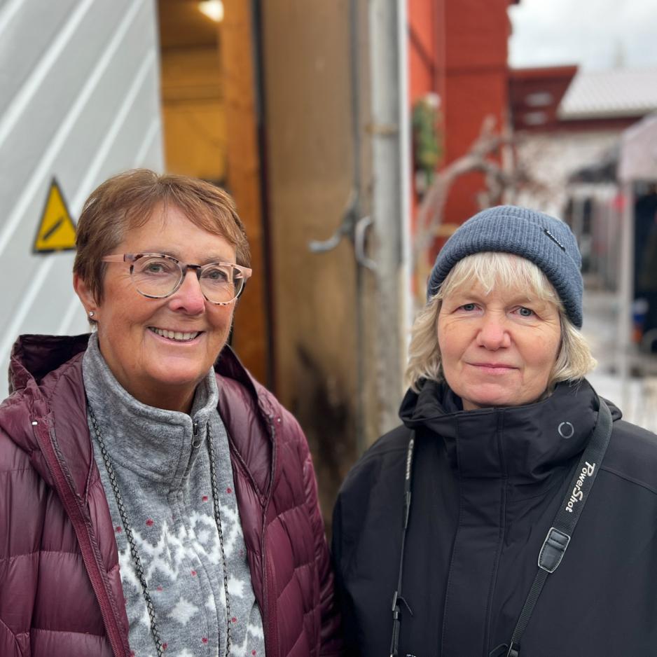 To kvinner som står sammen. Anne-Brit til venstre i lilla jakke, brunt kort sveis og briller. Trine Nevrum til høyre med hvit pannelugg, svart lue og jakke. Begge smiler