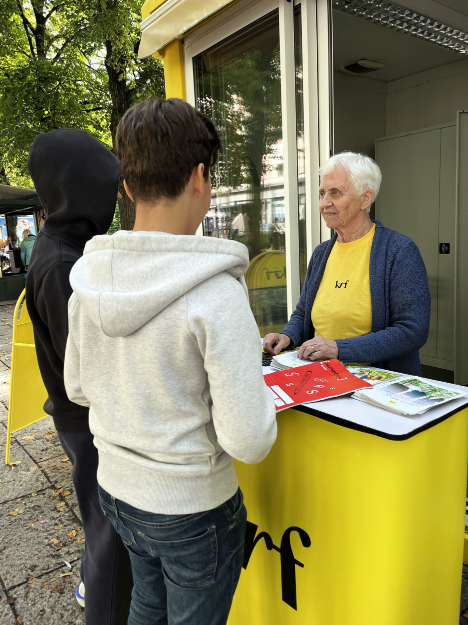 Dame som står på stand for krf og snakker med to gutter om politikken deres