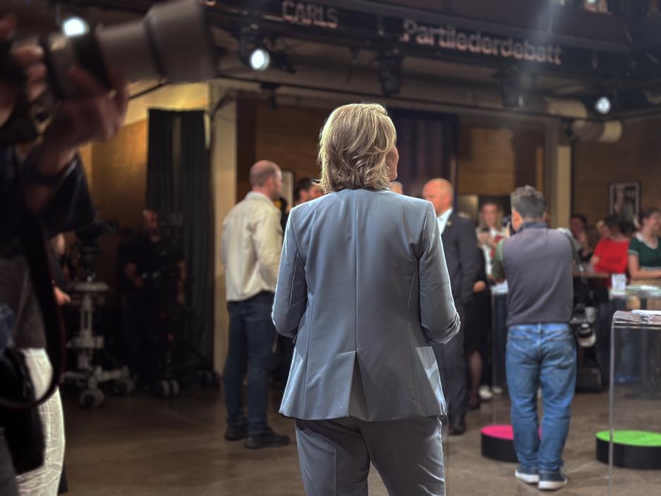 Sylvi Listhaug (Frp) står med ryggen til kamera under TV 2s partilederdebatt i Oslo. Hun har på seg en lys buksedress. Rundt henne er fotografer, TV-team og tilskuere samlet.