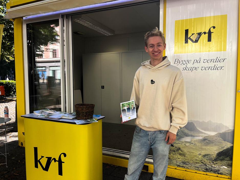 Gutt som står foran KrF stand med partiprogram i hånden
