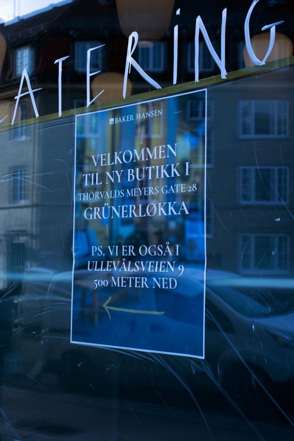 Bildet viser et nærbilde av et vindu med hvit håndskrevet tekst der ordet «CATERING» er delvis synlig øverst, og en blå plakat som informerer om ny butikk på Grünerløkka og adresse i Ullevålsveien. 