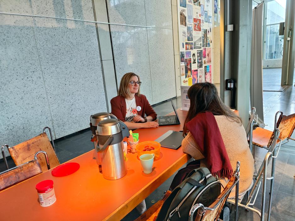 To damer sitter ved et oransje bord. Pepperkaker. Kaffe. Grå glassbakgrunn.