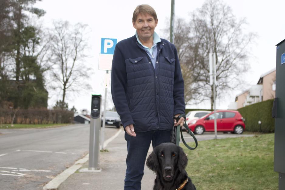 En mann og en svart hund ser rett inn i linsen. De står på fortauet. 