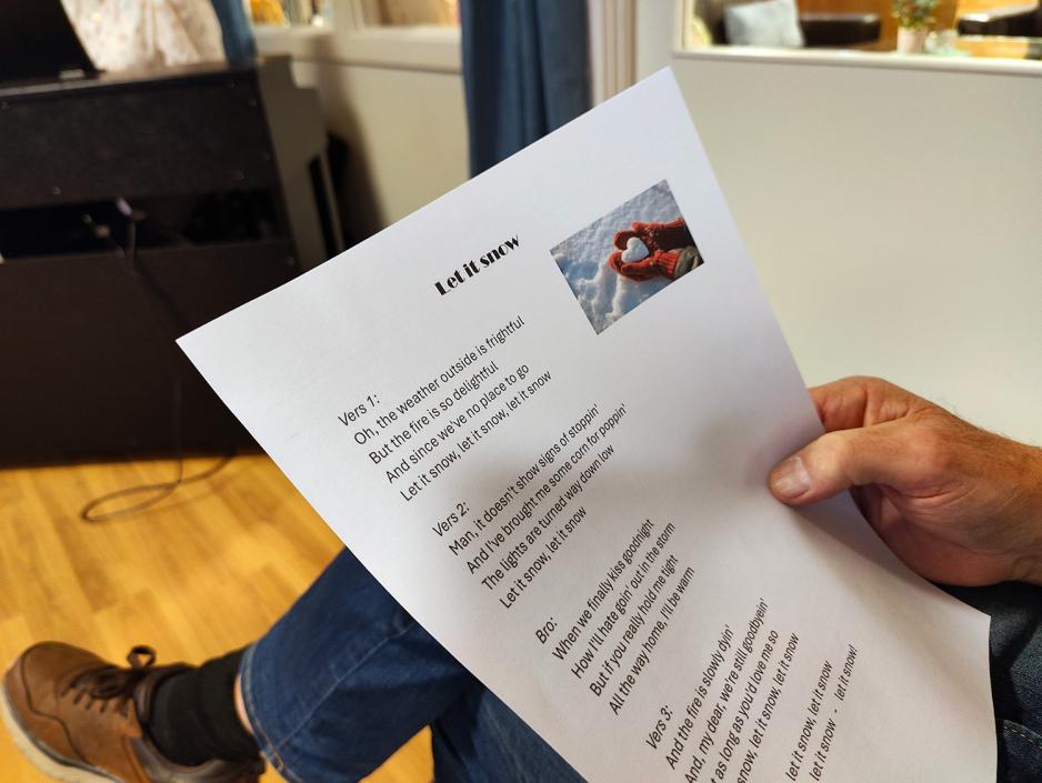 Sangtekst med Let it Snow. Ser en fot I bakken og en hånd som holder sangen.