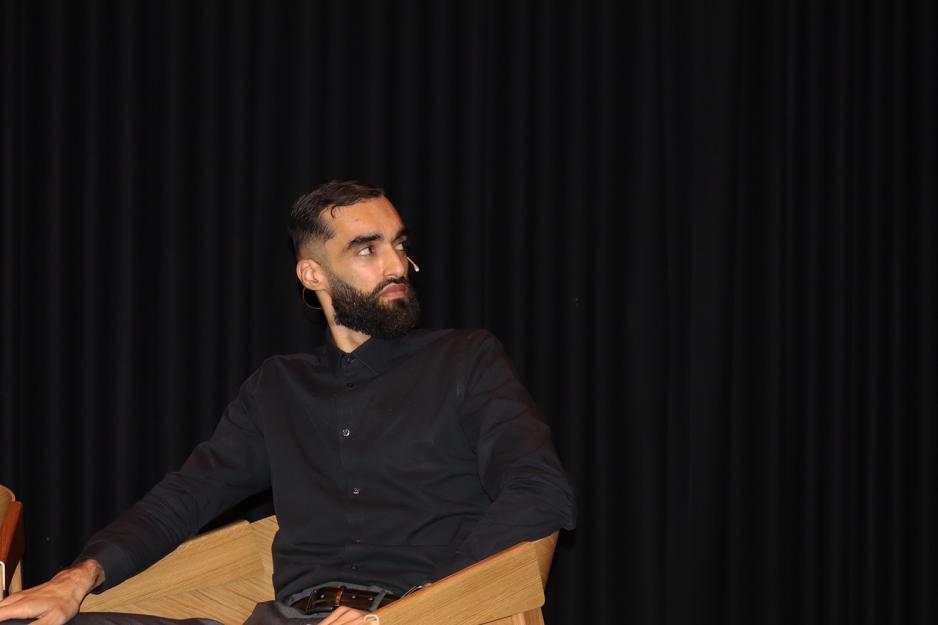 mann sitter i sort skjorte foran sort sceneteppe