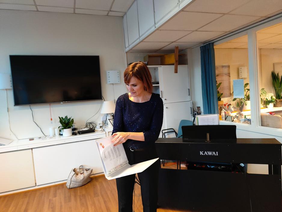 Korleder blar i korpermer. Bak henne er det et sort piano.