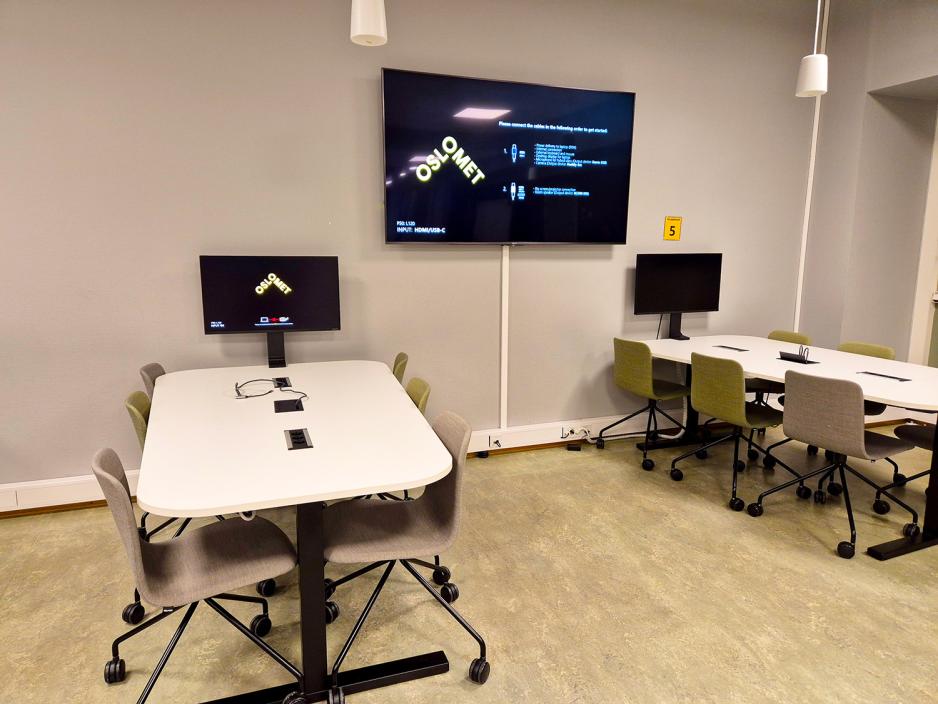 To bord med skjermer st&aring;r ved en vegg, og mellom dem er det en sort skjerm.