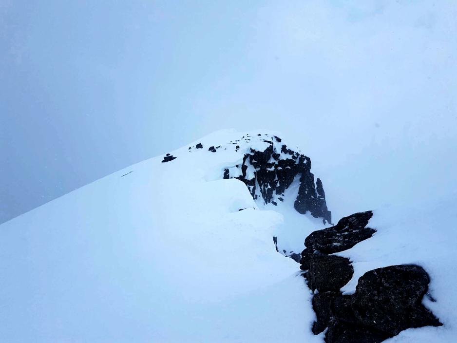 Sn&oslash; p&aring; toppen av et fjell. T&aring;ke i bakgrunnen
