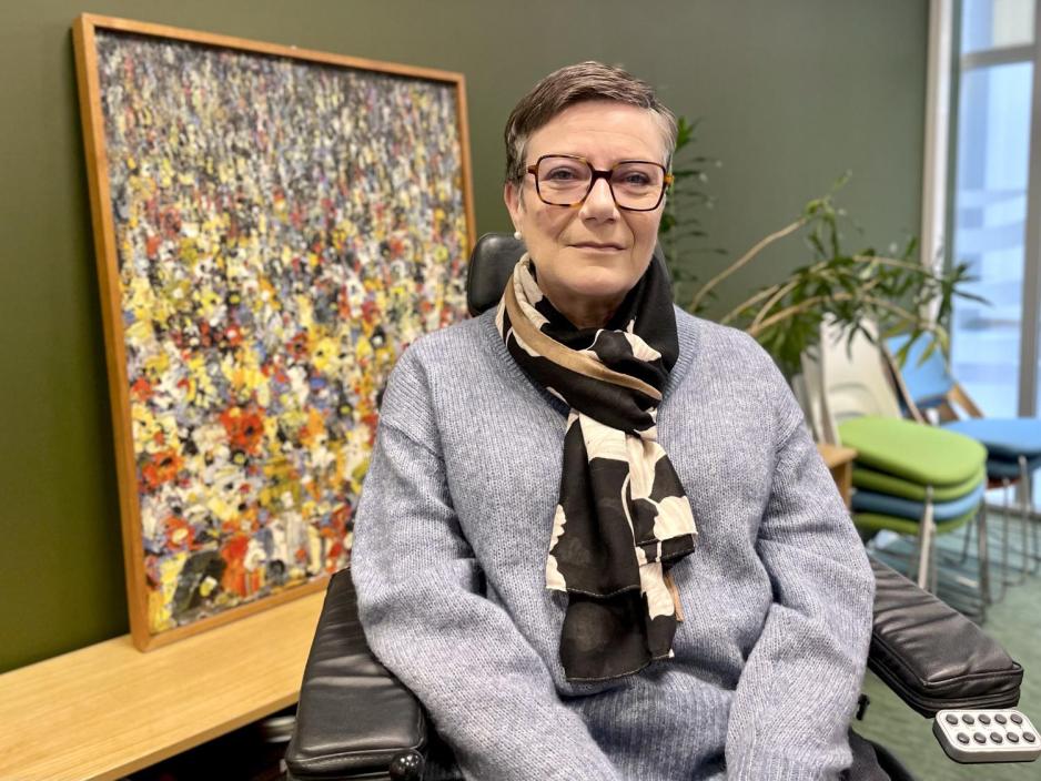 Kvinne sitter foran en gr&oslash;nn vegg.