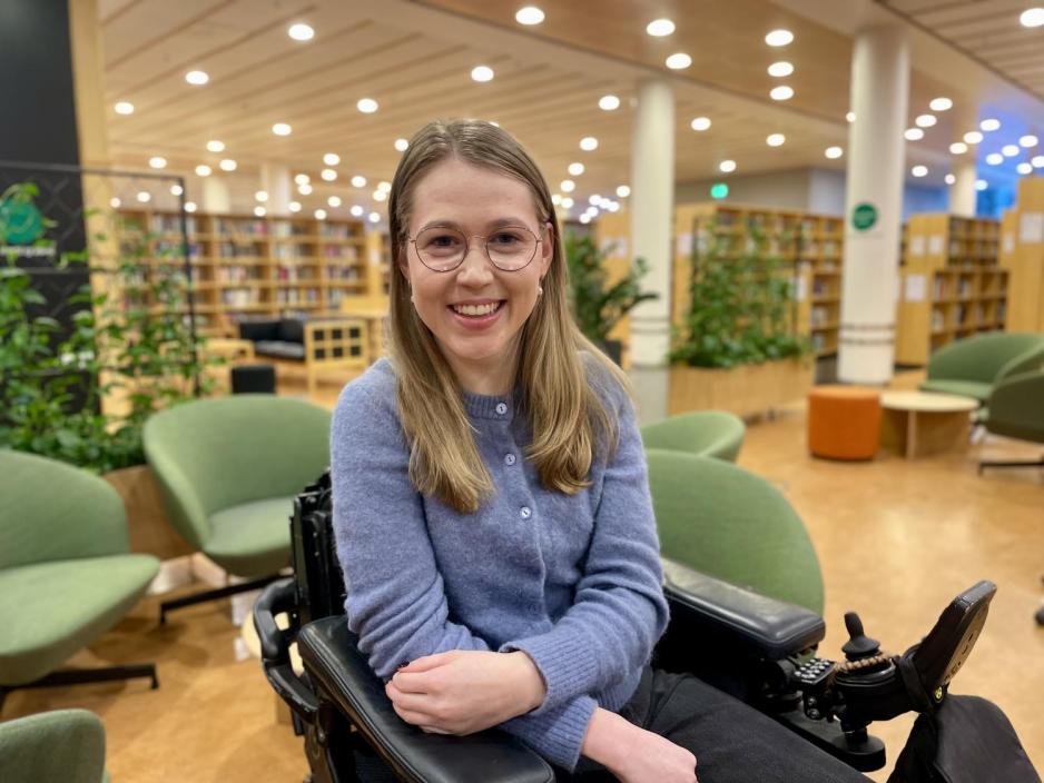 Kvinne i rullestol sitter og smiler.