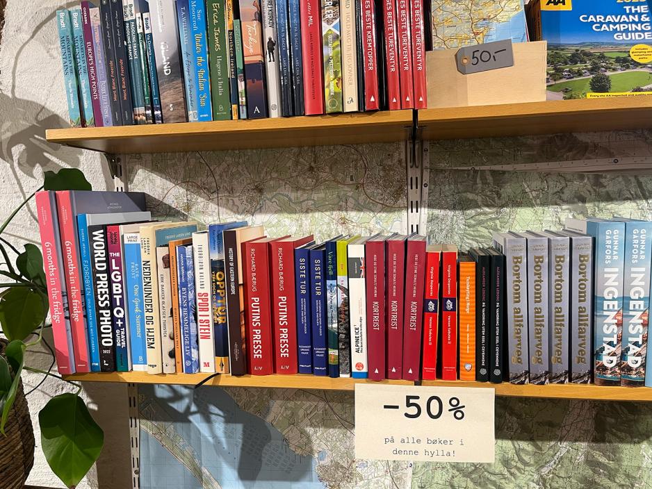 En bokhylle med reiseb&oslash;ker og et skilt med femti prosent rabatt.