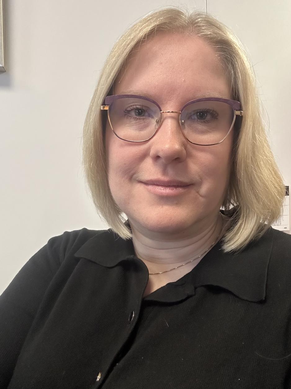 Kvinne med blondt h&aring;r og briller smiler.