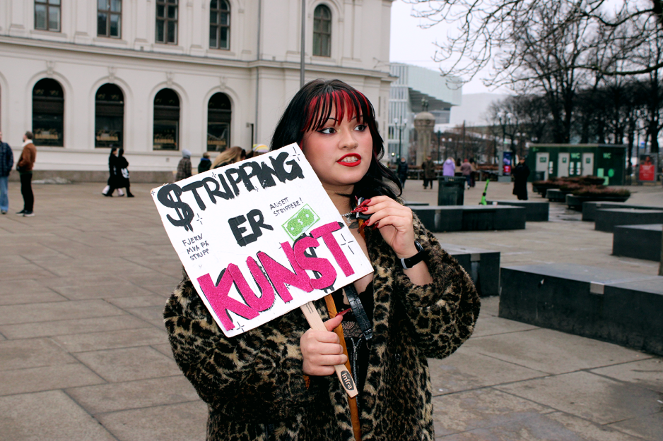 Stripper Alma Adoreholder en plakat der det st&aring;r "Stripping er Kunst"