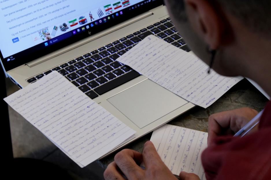 Mann skriver p&aring; papirer foran en PC-skjerm