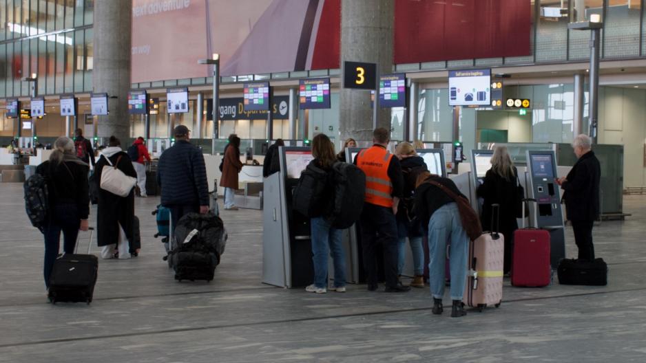 Lufthavnpresten hjelper en passasjer &aring; printe ut bagasjelapp