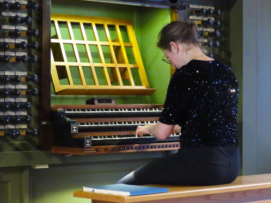 En svartkledd kvinne sitter og spiller orgel med ryggen til.