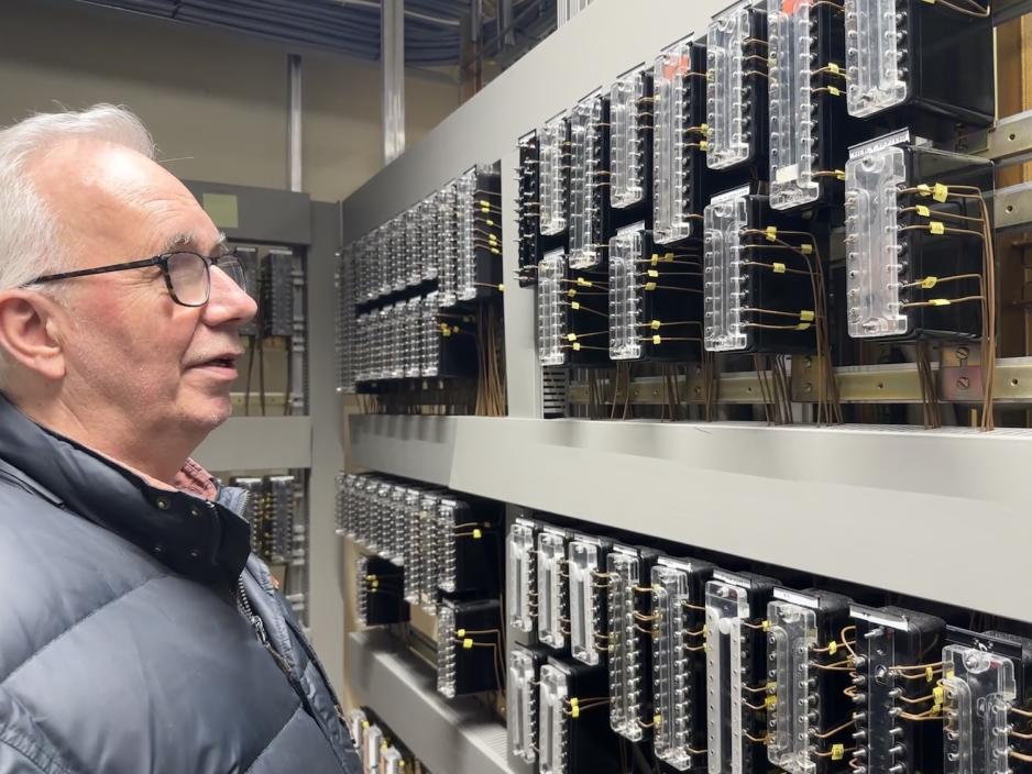 Kjell Holter st&aring;r foran en vegg med rel&eacute;er, han beskriver hvordan dette fungerer p&aring; stasjonen