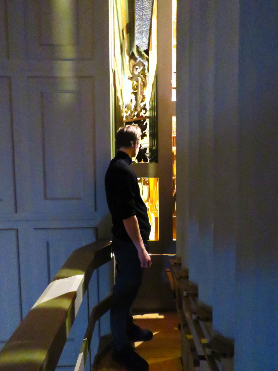 En svartkledd mann st&aring;r ved orgelmekanismen bak et orgel.