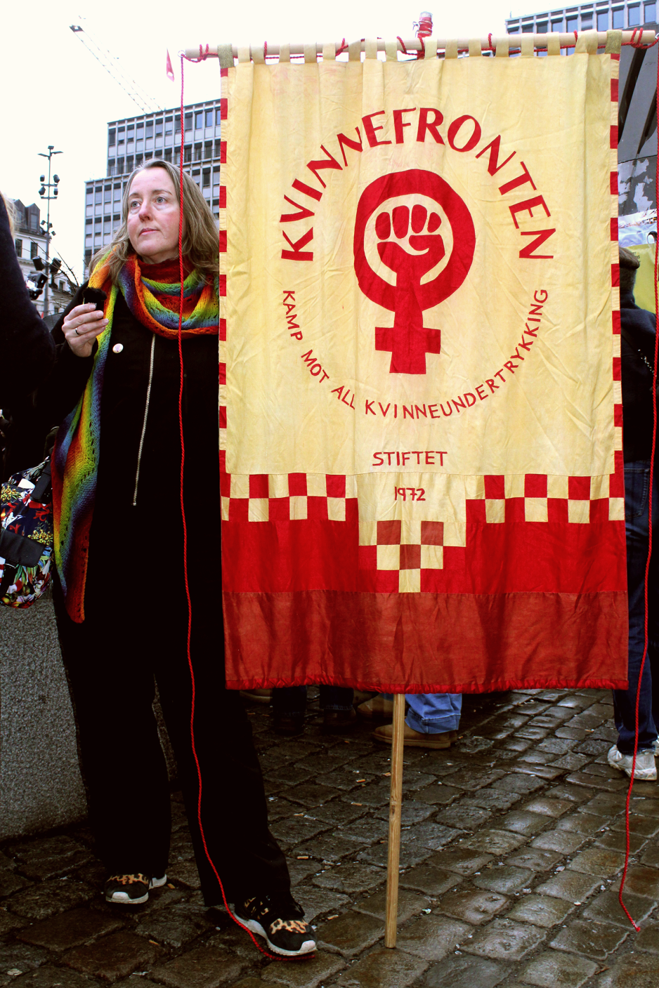 Trude Koksvik Nilsen fra Kvinnefronten st&aring;r vedsiden av banneret deres. Logoen har et kvinnetegn med en knyttneve, over st&aring;r teksten kvinnefronten