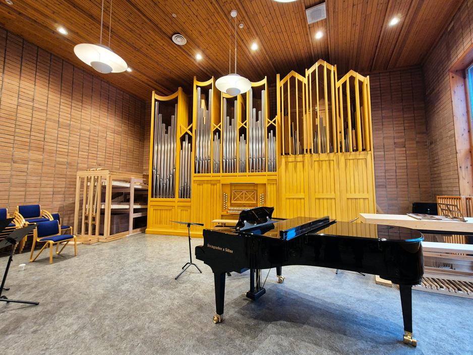 Stort klasserom med orgel i bakgrunnen og sort piano i forgrunnen.
