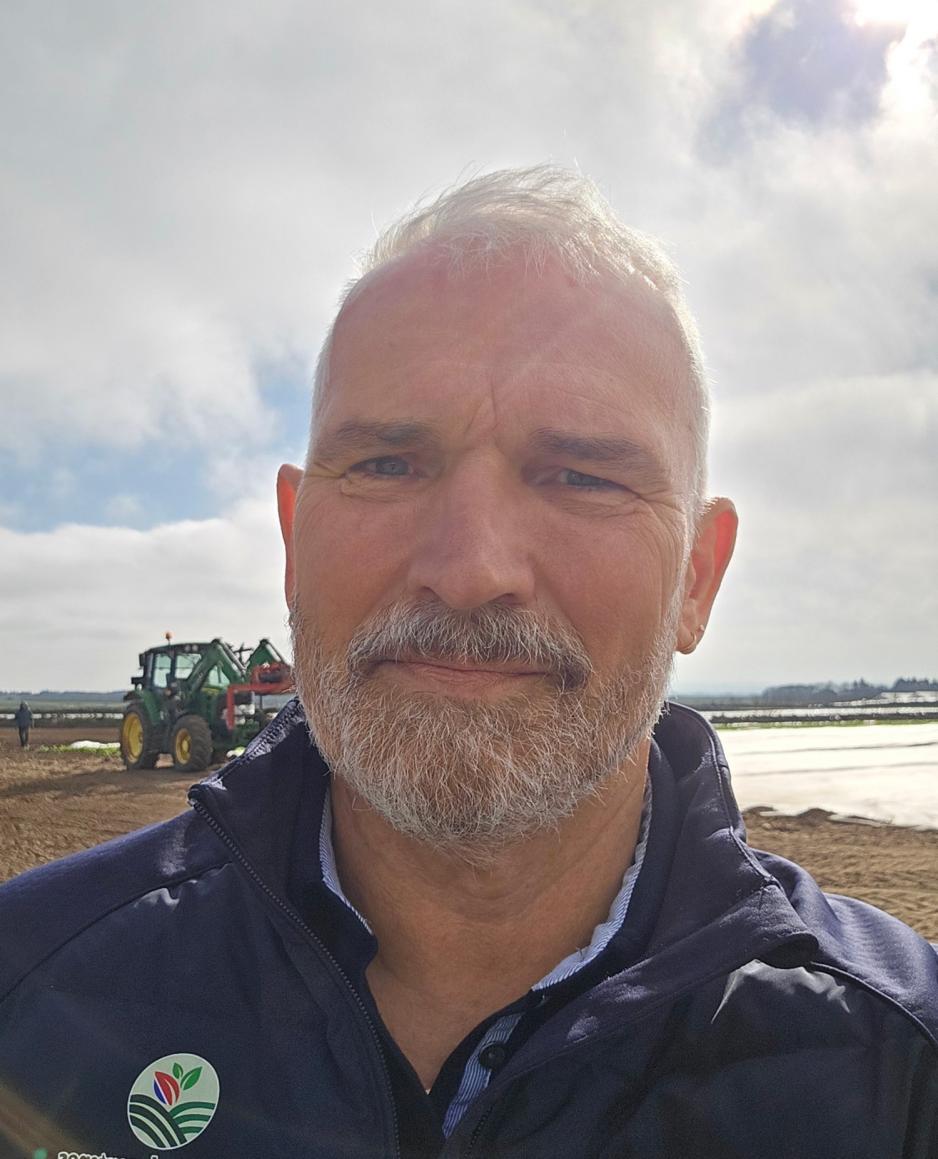 Bilde av Bjarte &aring;Sb&oslash; p&aring; en &aring;ker med en traktor i bakgrunnen.