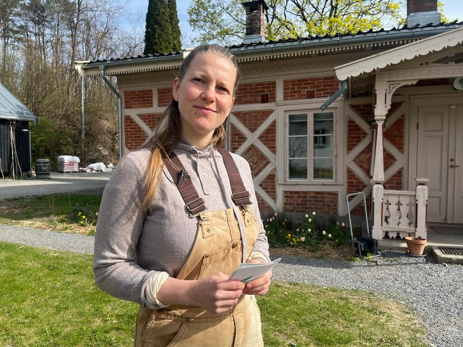 Hanne Rekve ser lurt i kameraet foran et pent, gammelt hus. 