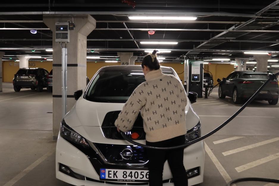 Jente som putter i laderen p&aring; sin bil 