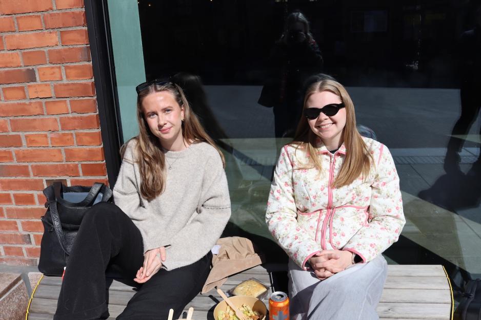 2 jenter som sitter p&aring; en benk i sola