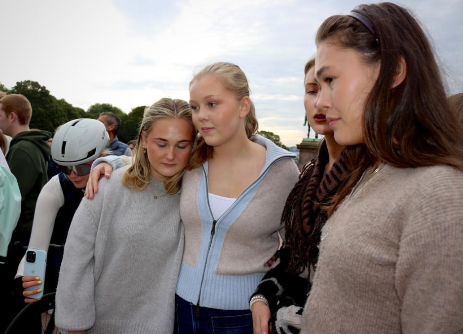 Fire unge kvinner står og ser bort på blomster. Hun ene holder rundt hun andre.