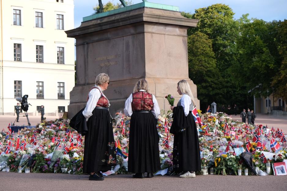 Damer i bunad legger ned blomster